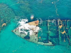 Explore the mysterious remnants of a sunken ship in the vibrant blue waters of the Dominican Republic from above.