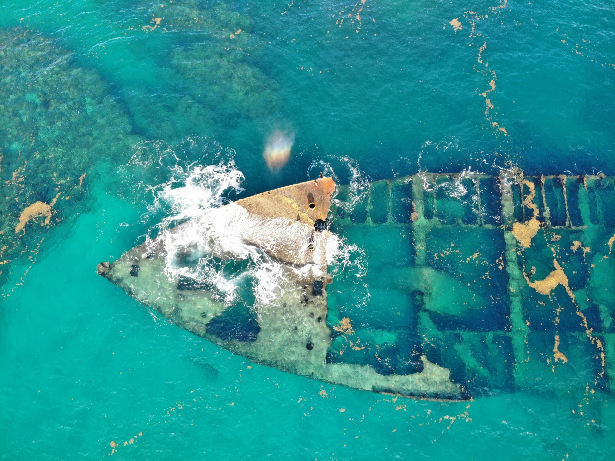 Explore the mysterious remnants of a sunken ship in the vibrant blue waters of the Dominican Republic from above.